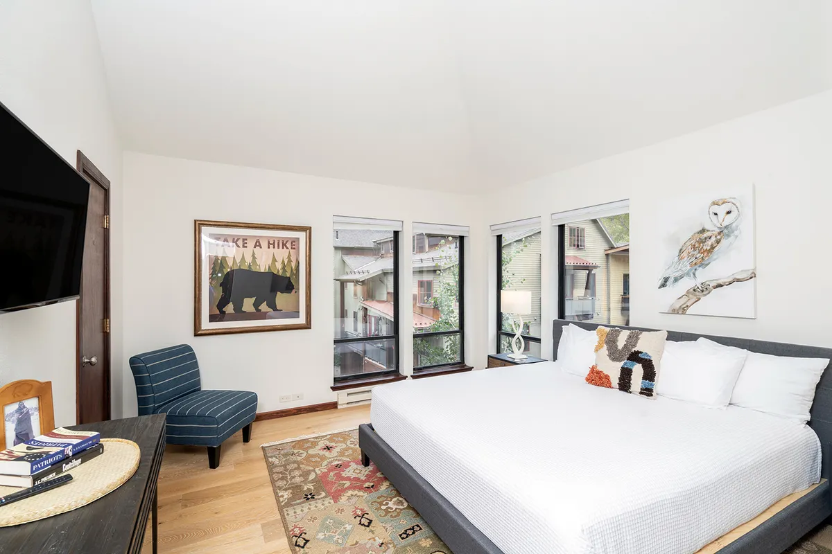 A spacious and serene bedroom featuring a large king bed with plush bedding, calming artwork above the headboard, and a window that fills the room with natural light. The tranquil atmosphere is ideal for unwinding, and the space exudes a sense of privacy and comfort—perfect for a master suite.