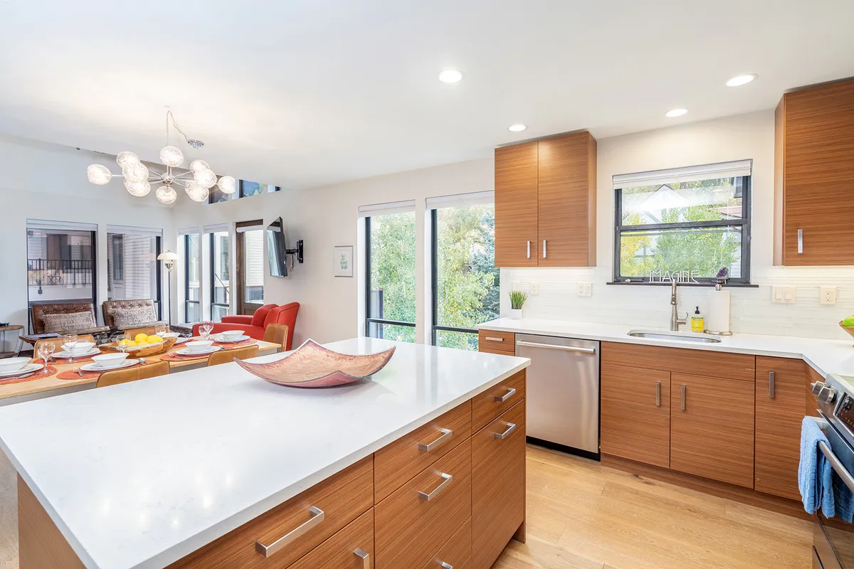 A bright, open kitchen with a large island, modern light fixture, and an adjacent dining area. The space is enhanced by large windows that allow natural light to flood in, making it ideal for both casual breakfasts and festive gatherings.