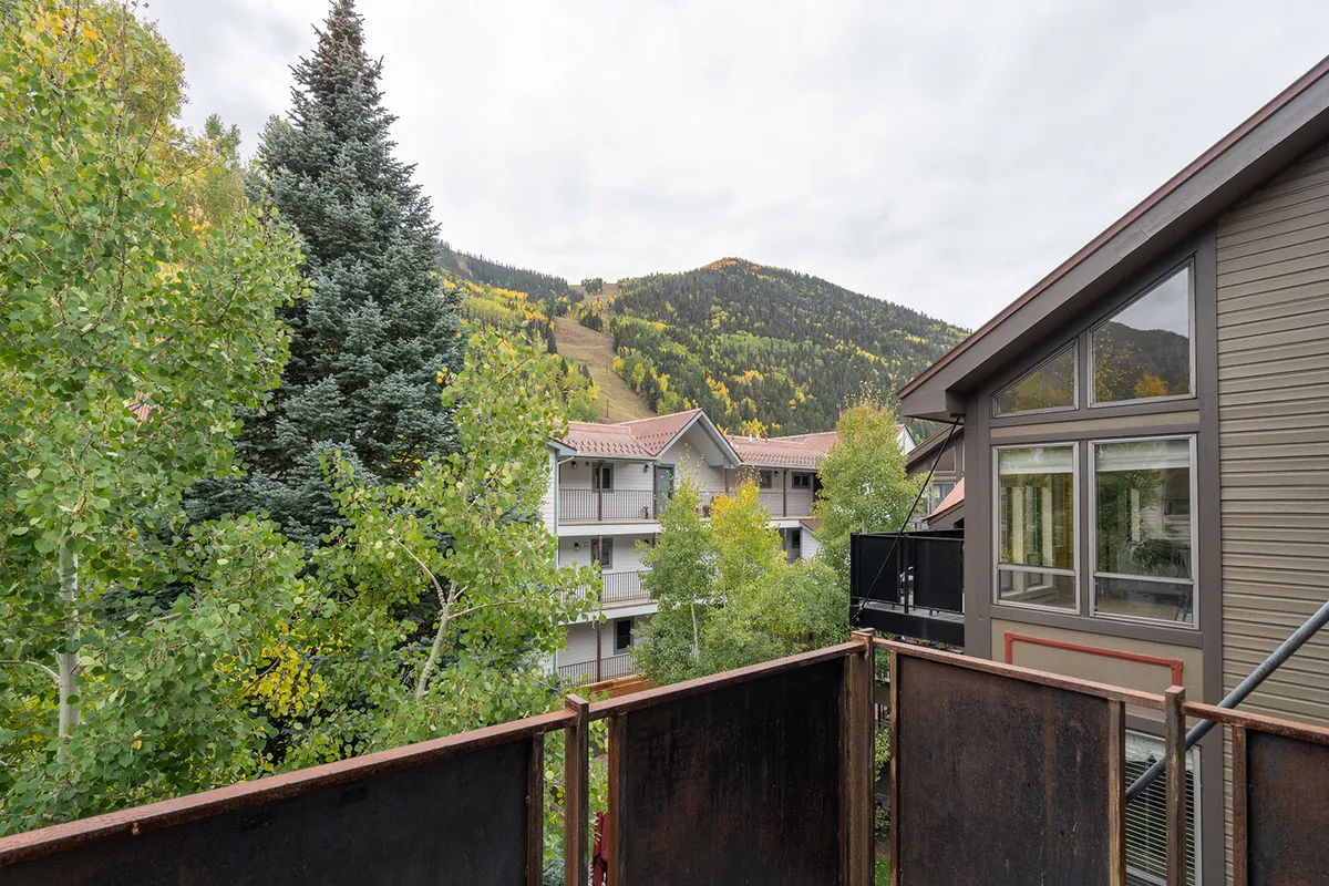 A peaceful mountain view from a balcony with tree foliage and charming building architecture in the frame, inviting moments of relaxation and appreciation for the stunning natural surroundings.