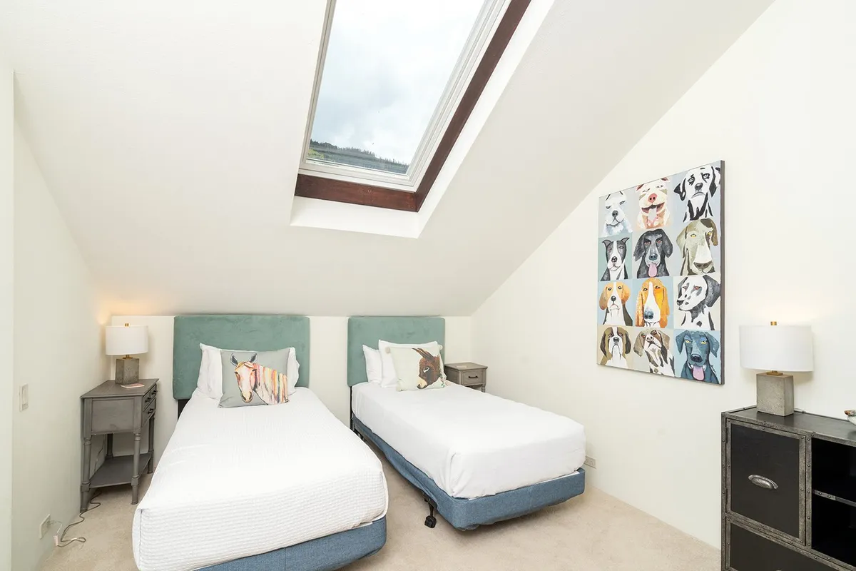 An inviting upstairs bedroom with twin beds, playful dog-themed artwork, a skylight that bathes the room in light, and a cozy, playful vibe. The flexible sleeping arrangement is suitable for families or groups and the whimsical decor adds character and comfort.